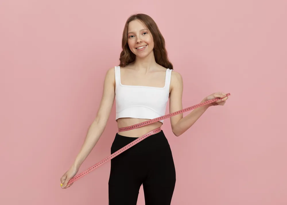 uśmiechnięta kobieta mierzy obwód brzucha ponieważ udało jej się spalić tłuszcz z brzucha