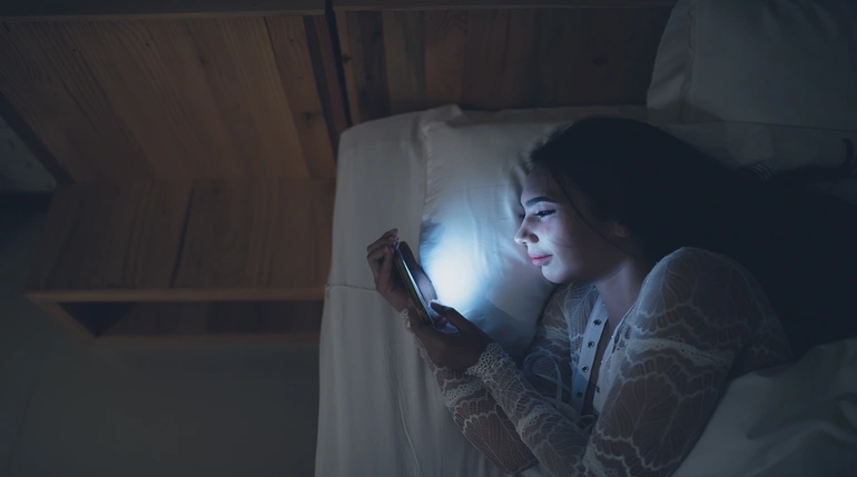 kobieta wpatrująca się w smartfon w nocy