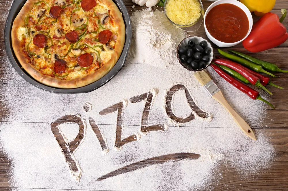 gotowa pizza i napis pizza na rozsypanej mące
